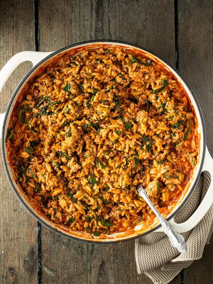 Orzo Pfanne mit Hackfleisch und Spinat auf einem dunklen Holzuntergrund.