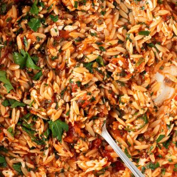 Cremiges Orzo Risotto mit geriebenem Halloumi, Tomate und Petersilie in einer Pfanne.