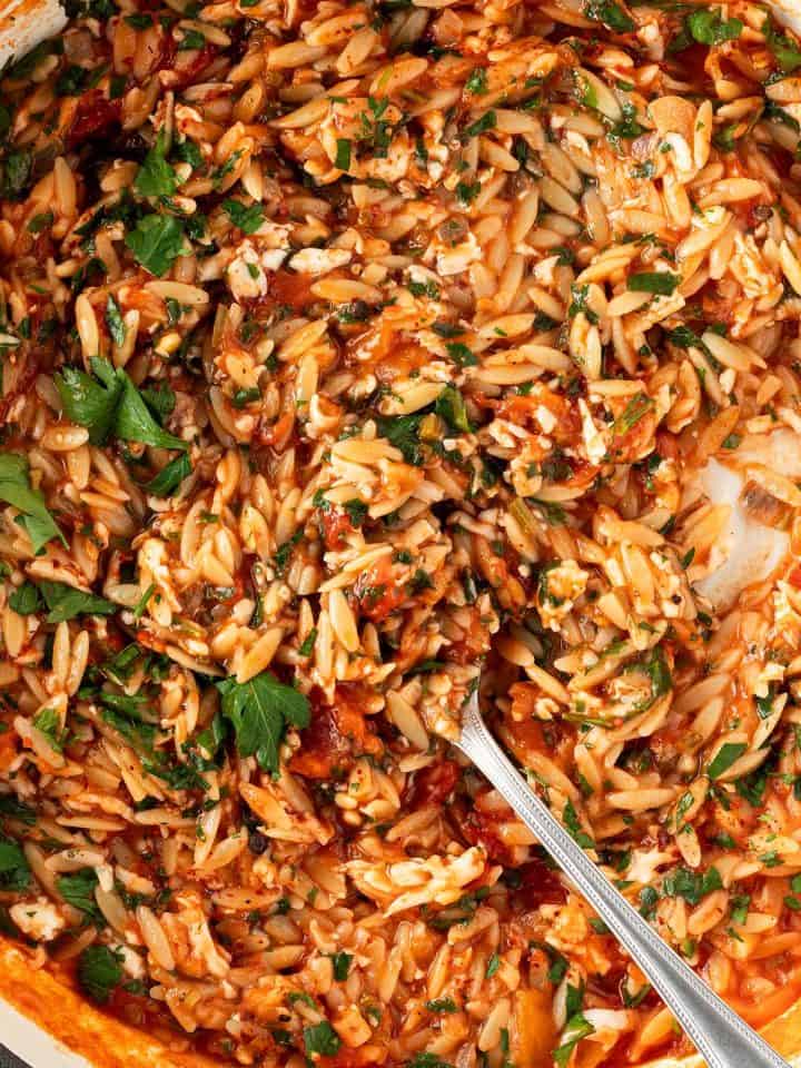 Cremiges Orzo Risotto mit geriebenem Halloumi, Tomate und Petersilie in einer Pfanne.