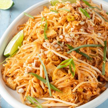 Pad Thai mit Tofu serviert auf einem gro&szlig;en Teller mit Fr&uuml;hlingszwiebeln und Limetten.