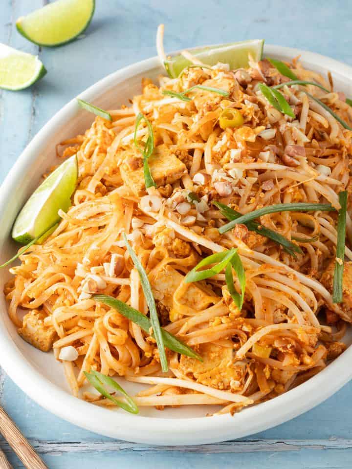 Pad Thai mit Tofu serviert auf einem gro&szlig;en Teller mit Fr&uuml;hlingszwiebeln und Limetten.