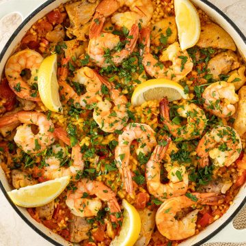 Paella mit H&auml;hnchen und Garnelen, garniert mit frischer Petersilie und Zitronenspalten, in einer gro&szlig;en Pfanne.