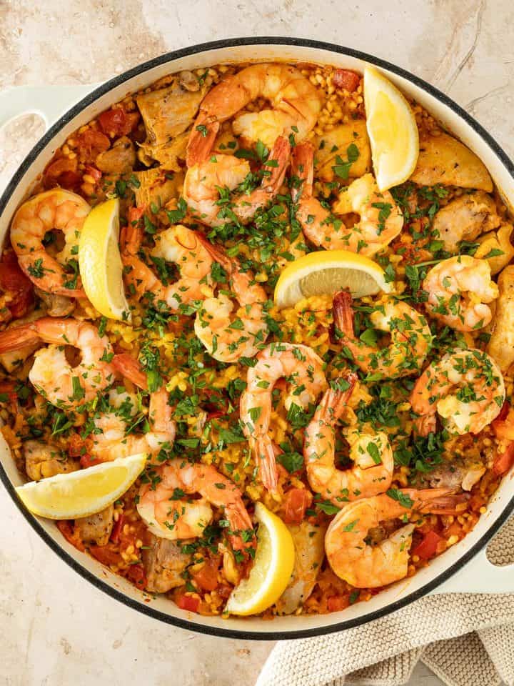 Paella mit Hähnchen und Garnelen, garniert mit frischer Petersilie und Zitronenspalten, in einer großen Pfanne.