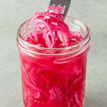 Ein Glas mit eingelegten Zwiebeln, wo eine Gabel ein paar Zwiebelringe rausholt.