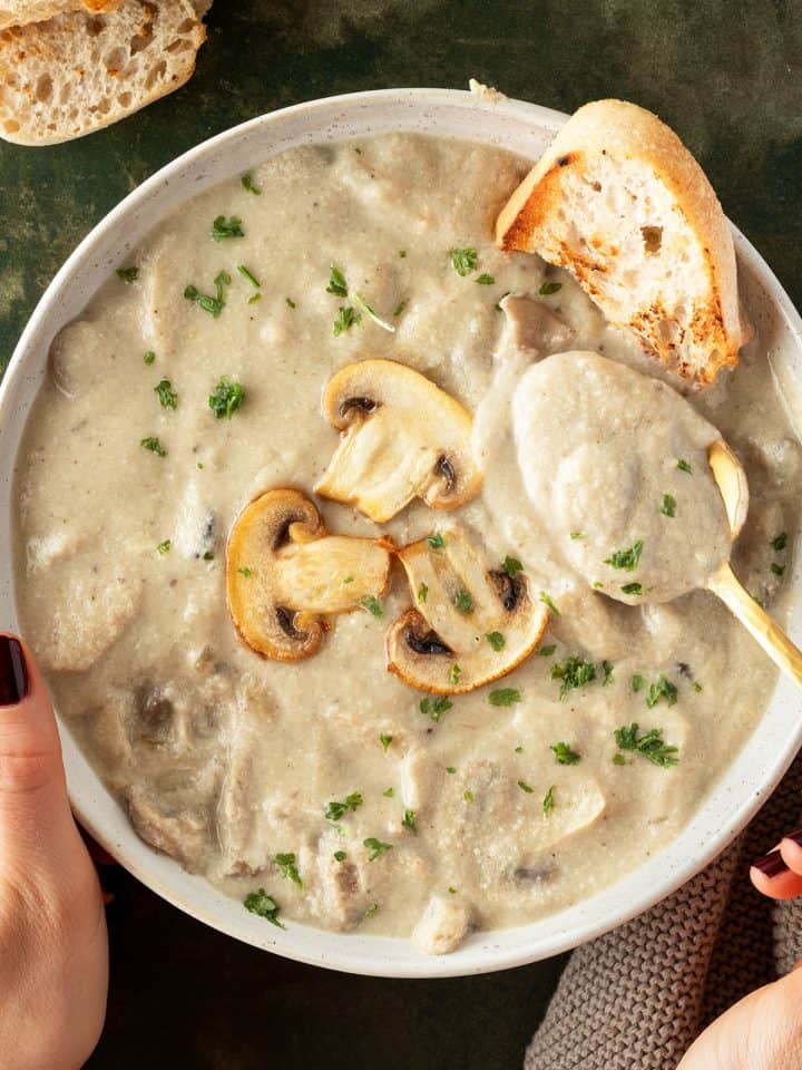 Eine Sch&uuml;ssel mit cremige Pilzzsuppe serviert mit knusprigem Brot, in der ein L&ouml;ffel eingetunkt wurden.