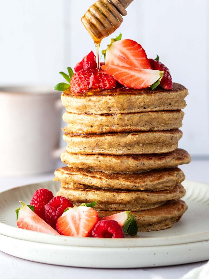 Auf einen Stapel aus Pancakes mit frischen Beeren wird Honig geträufelt.