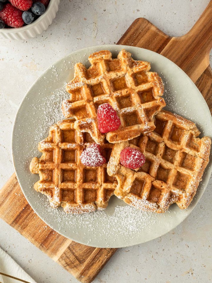 Drei dicke, fluffig Waffeln auf einem Teller mit Puderzucker, Beeren und Sirup serviert.