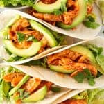 F&uuml;nf nebeinander liegende Tacos mit H&auml;hnchen in einer w&uuml;rzigen Sauce, Avocado und Salat.