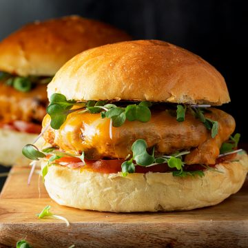 Zwei Puten Burger mit frischen Sprossen und Tomate auf einem Holzbrett vor dunklem Hintergrund.