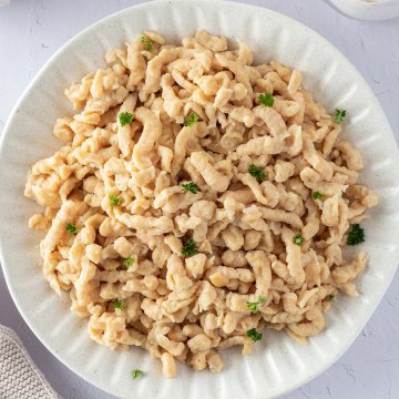 Vogelperspektive auf einen Teller mit Quarkspätzle mit frischer Petersilie und Deko im Bildrand.