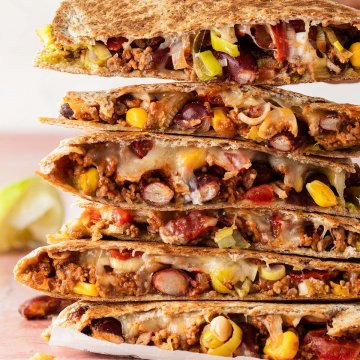 Ein Stapel Quesadilla mit Hackfleisch, wo eine Hand einen Quesadilla wegnimmt.