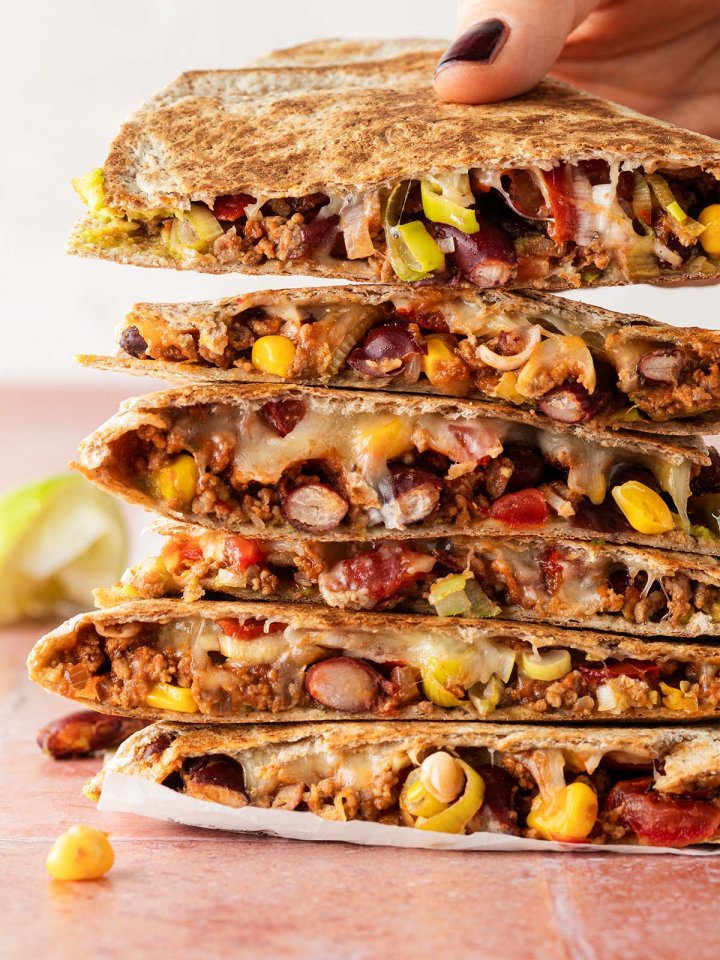 Ein Stapel Quesadilla mit Hackfleisch, wo eine Hand einen Quesadilla wegnimmt.