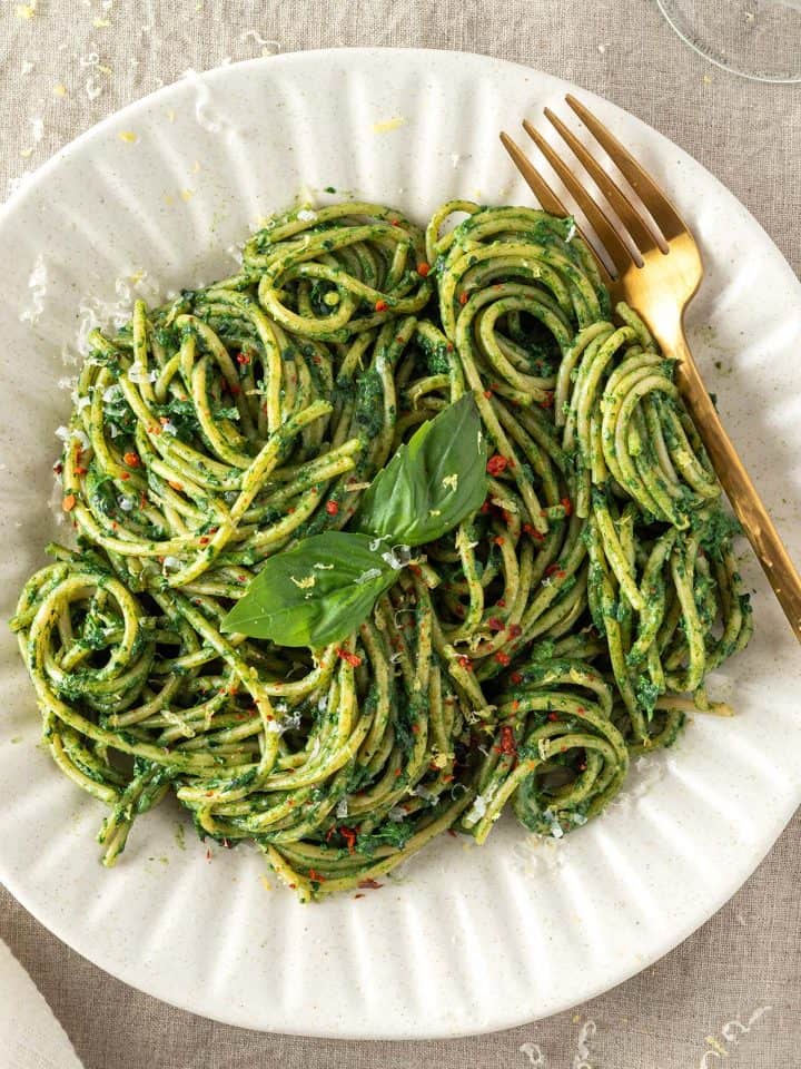 Ein gedeckter Tisch auf dem ein Teller mit Spaghetti mit grüner Sauce serviert werden.