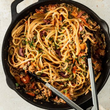 Spaghetti Puttanesca serviert in einer Gusseisenpfanne, Deko im Bildrand.