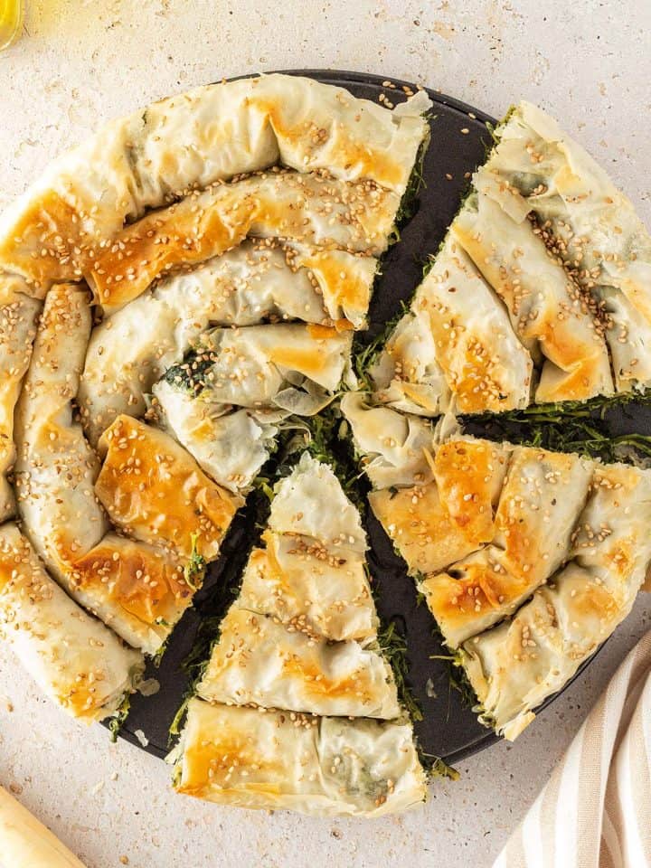 Goldbraun gebackener, griechischer Spinatstrudel, der zur Hälfte angeschnitten ist.