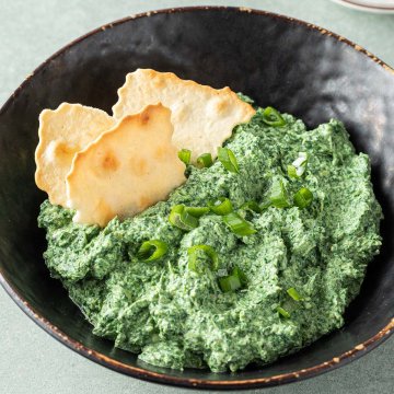 Cremiger Spinatdip in einer Sch&uuml;ssel mit Fr&uuml;hlingszwiebeln und Crackern serviert.