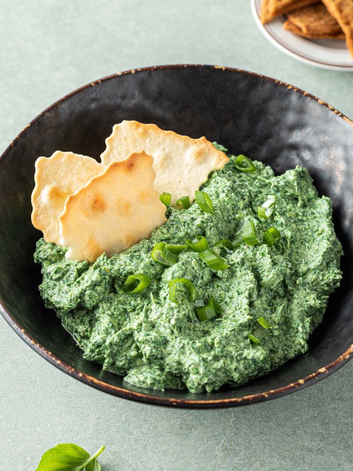 Cremiger Spinatdip in einer Schüssel mit Frühlingszwiebeln und Crackern serviert.