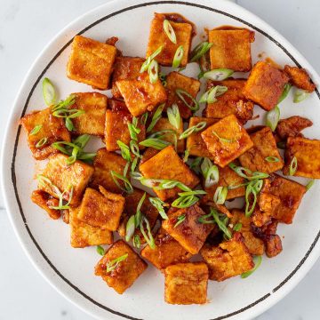 Knusprige Tofu-St&uuml;cke mit einer Sticky s&uuml;&szlig;-sauer Sauce auf einem Teller mit Fr&uuml;hlingszwiebeln.