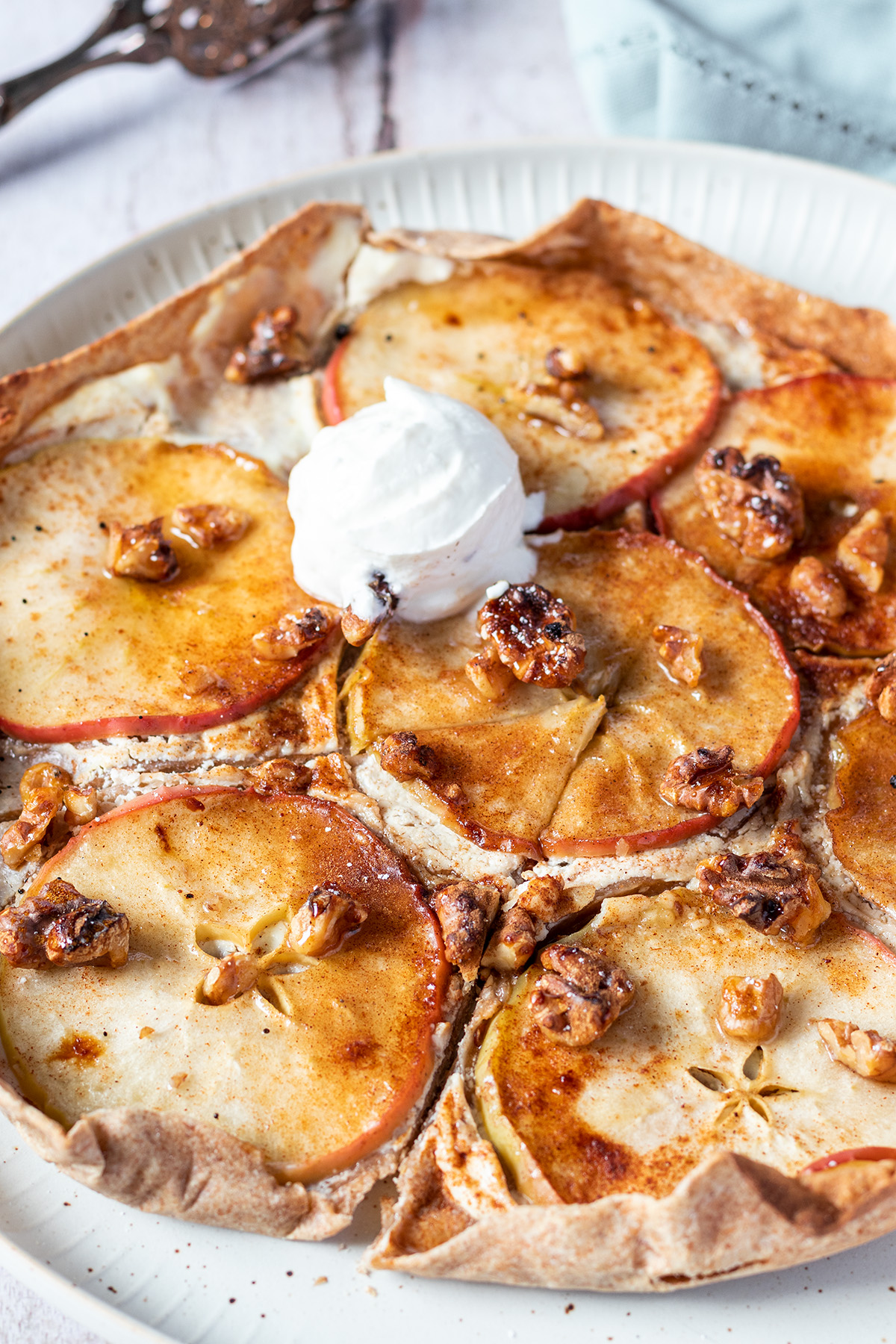 Süßer Flammkuchen mit in Scheiben geschnittenen Äpfeln, Ricotta und Walnüssen belegt und mit etwas Eis serviert.