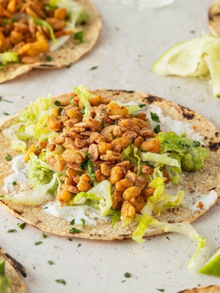 Veganer Taco mit knusprigen Tempeh und Salat, Limetten und weitere Tacos im Bildrand.