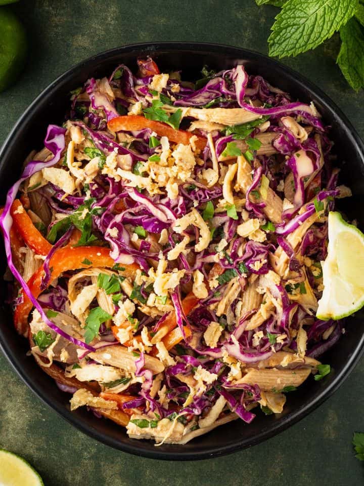 Ein Teller Thai Crunch Salat mit Rotkohl, Nudeln, Gemüse, Hähnchen und Röstzwiebeln, Deko im Hintergrund.