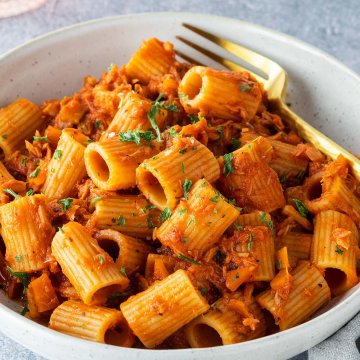Ein Teller mit Rigatoni in einer Thunfisch-Toamtensoße auf einem hellgrauen Untergrund.