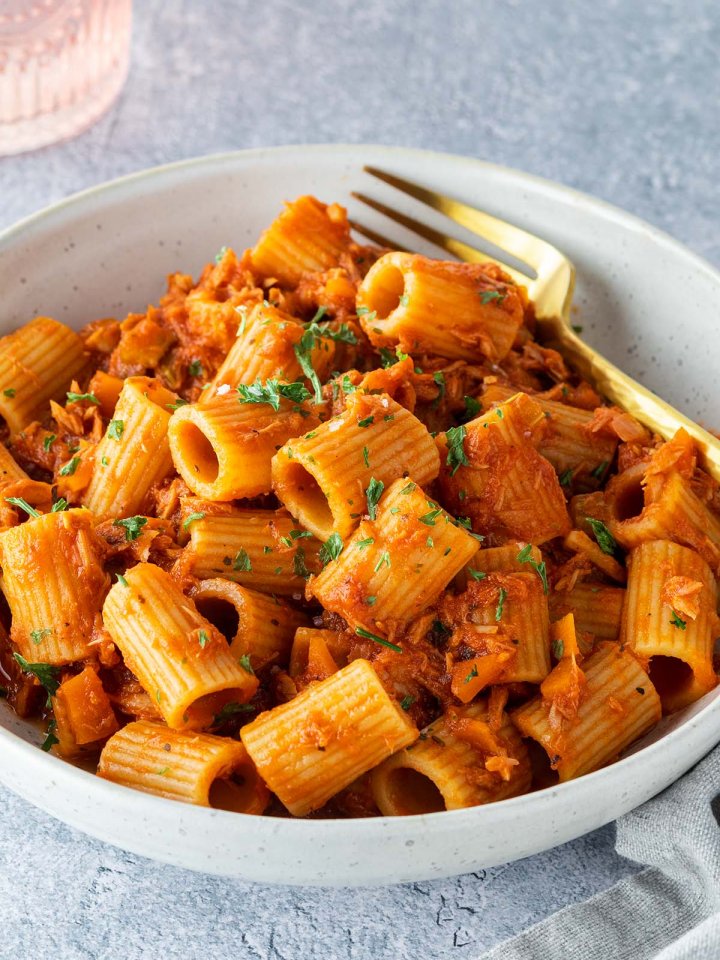 Ein Teller mit Rigatoni in einer Thunfisch-Toamtensoße auf einem hellgrauen Untergrund.