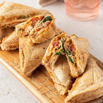 Acht warme Thunfisch Sandwiches auf einem Holzbrett, zwei davon in der Mitte halbiert.