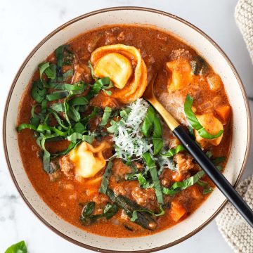 Sch&uuml;ssel mit cremiger Tortellini Suppe auf hellem Untergrund.