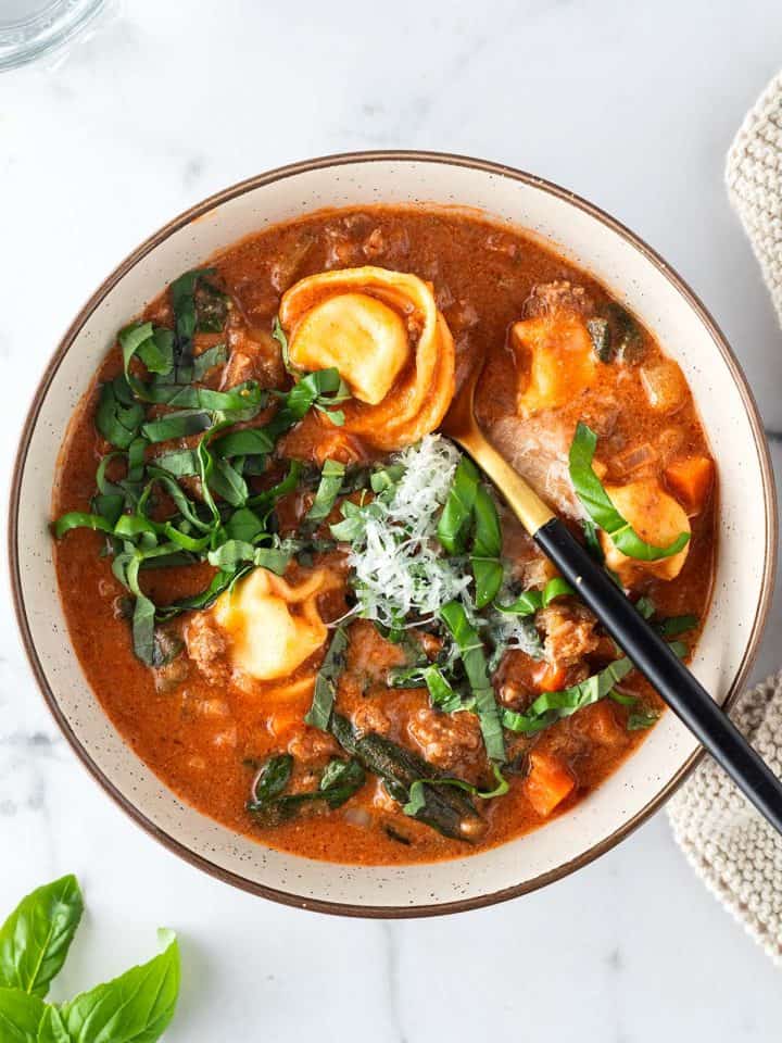 Sch&uuml;ssel mit cremiger Tortellini Suppe auf hellem Untergrund.