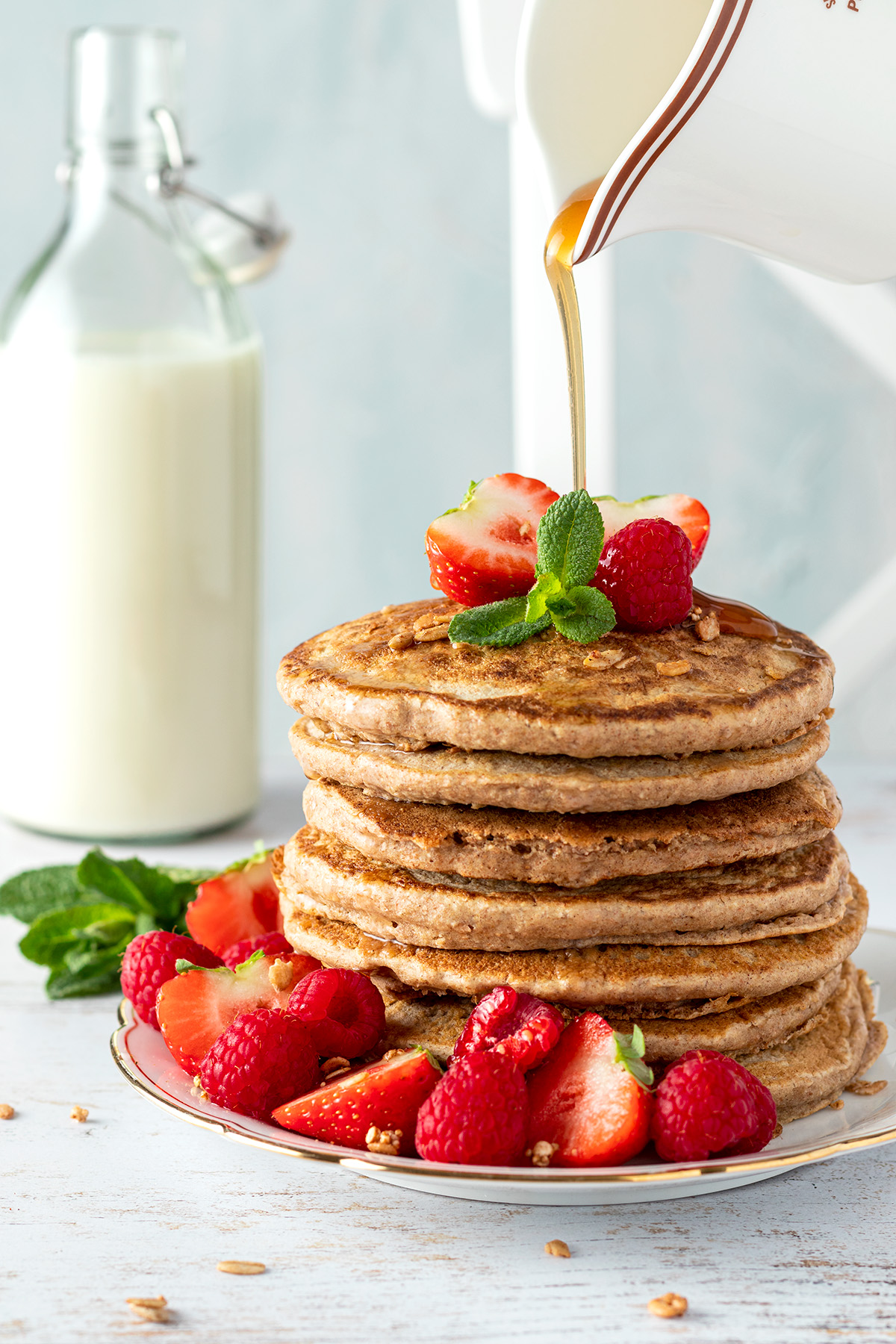 Ahornsirup wird auf die veganen Pancakes gegossen, die mit Himbeeren und Erdbeeren aufeinander gestapelt serviert werden