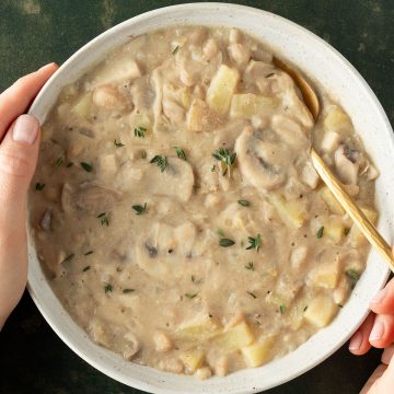 Wei&szlig;er Bohneneintopf mit Pilzen und Kartoffeln in einem tiefen Suppenteller.