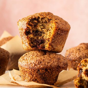 Zucchini Muffins mit saftiger Krume und geschmolzenen Schokostückchen, zwei davon aufeinander gestapelt, ein Muffin angebissen.