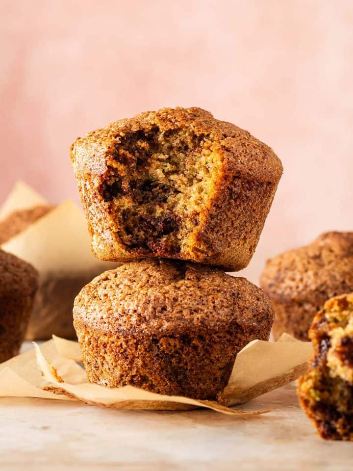 Zucchini Muffins mit saftiger Krume und geschmolzenen Schokost&uuml;ckchen, zwei davon aufeinander gestapelt, ein Muffin angebissen.
