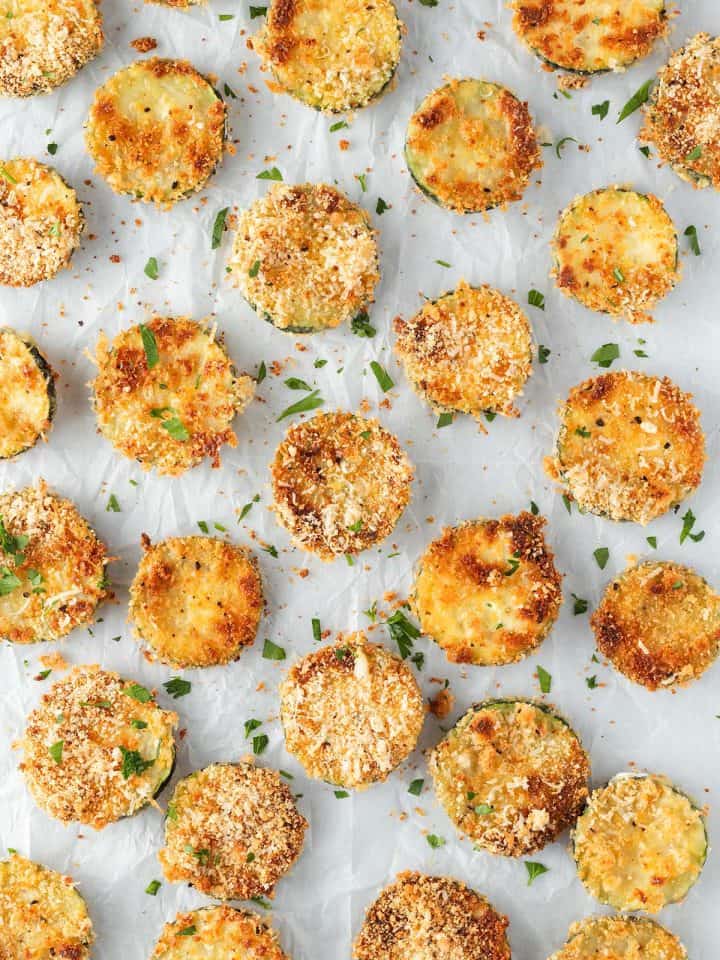 Knusprige Parmesan Zucchini Chips auf wei&szlig;em Backpapier.