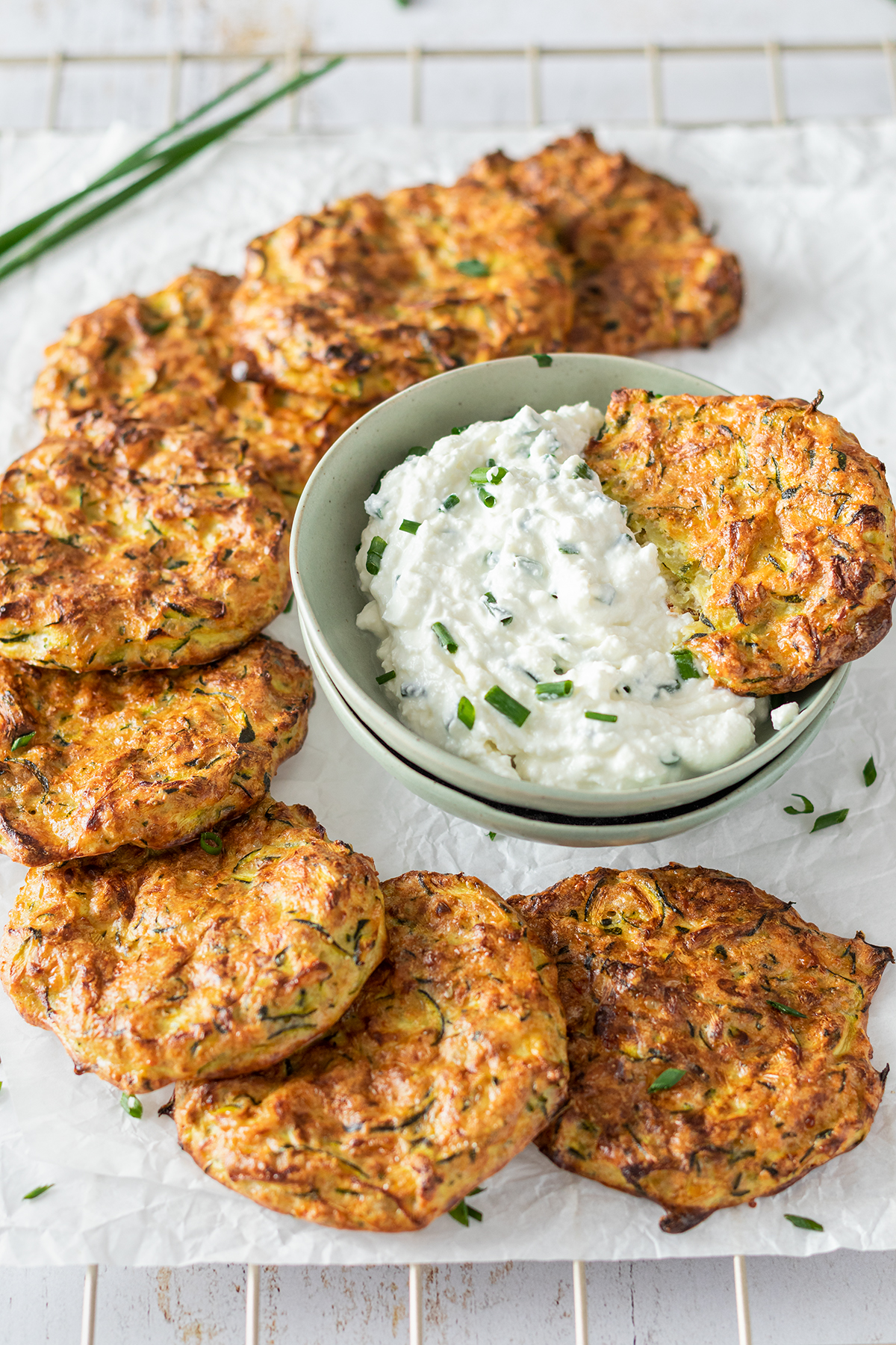 Knusprige Zucchinipuffer auf einem Auskühlgitter, serviert mit einem cremigen Dip.